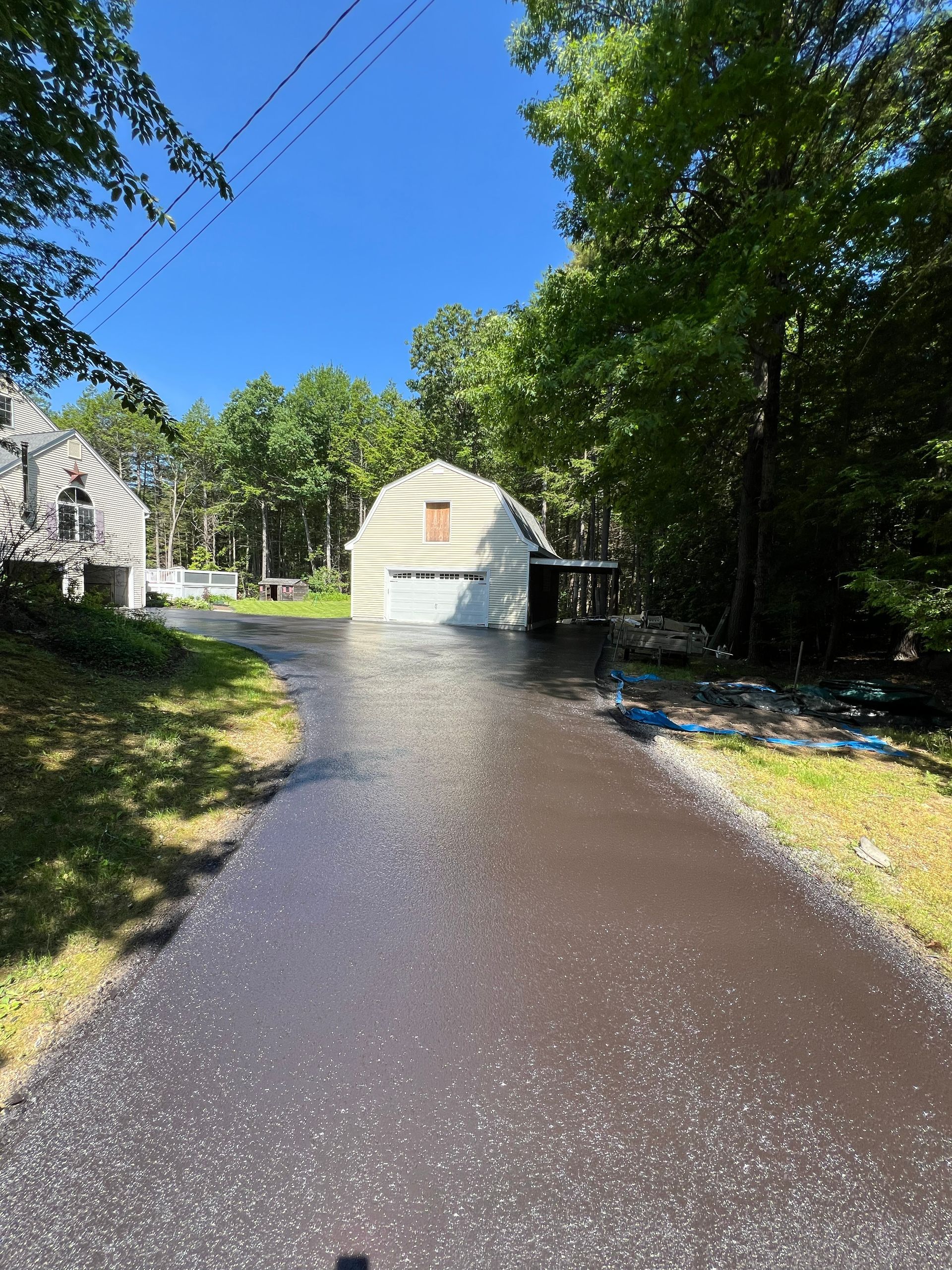 Driveway leading to a white garage with a carport under a clear blue sky. Trees surround the scene.