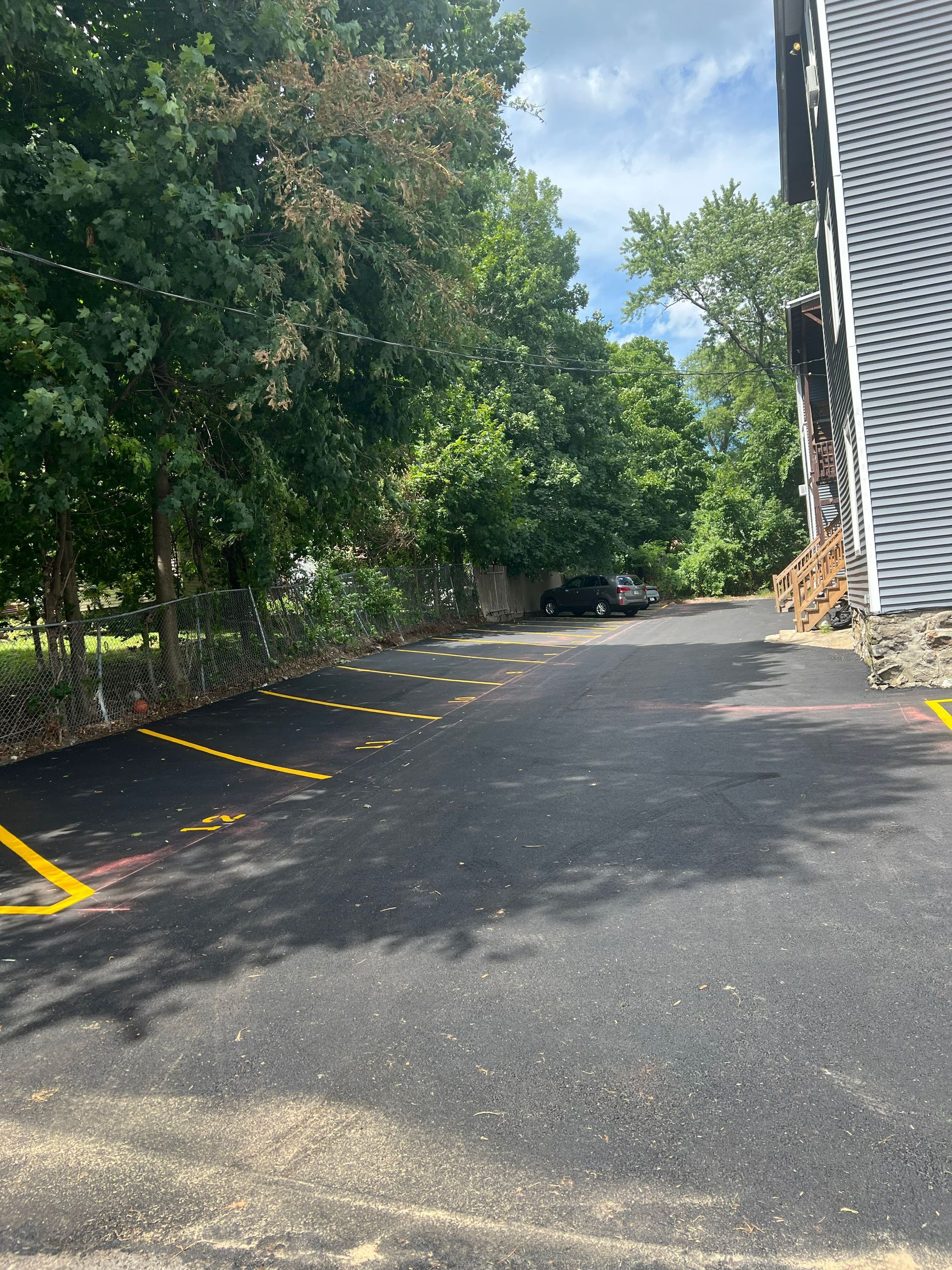 Asphalt parking lot with yellow painted parking spaces next to a building and trees.