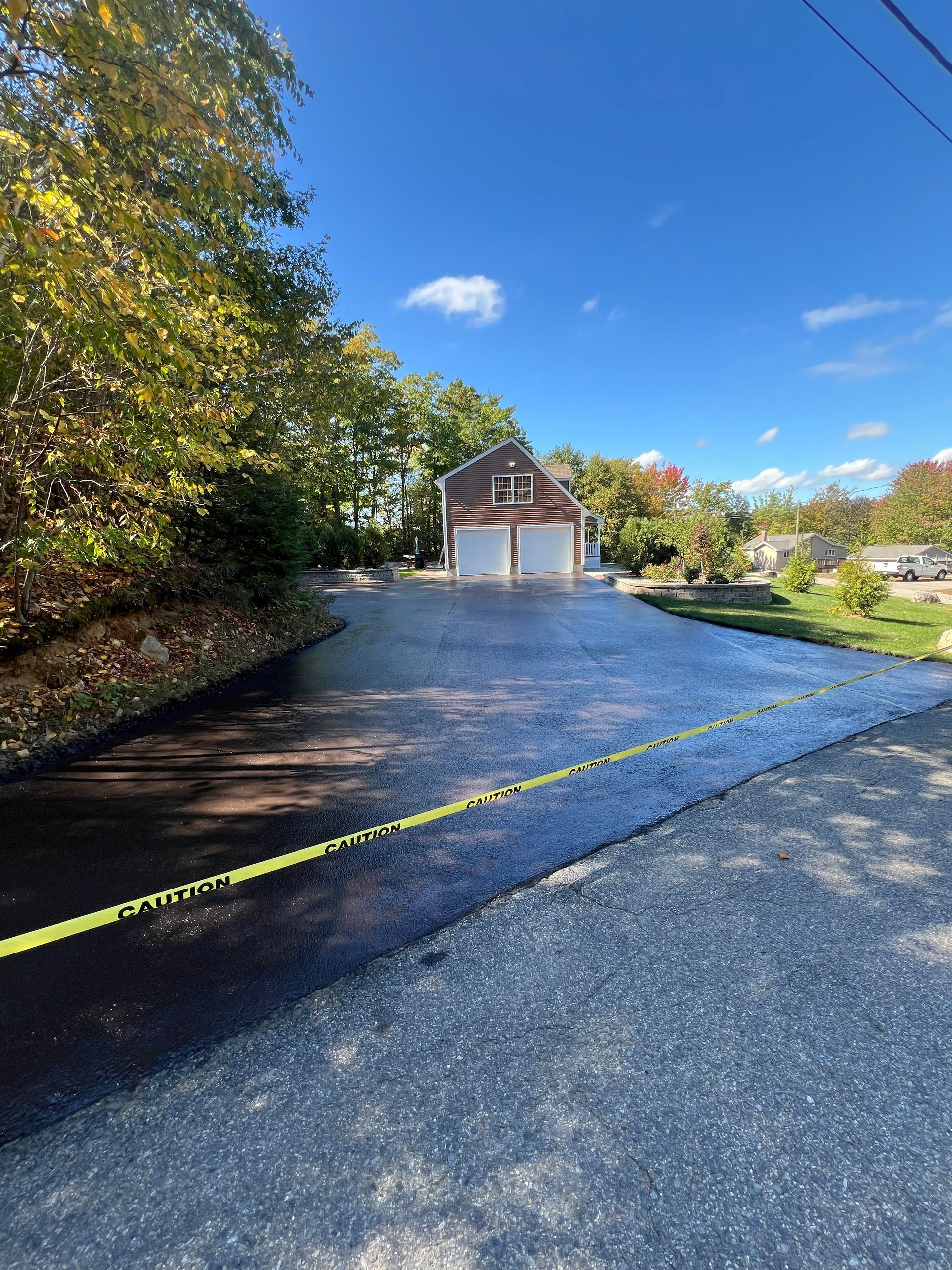 Newly paved driveway leading to a two-car garage with the sky in the background, yellow tape across the driveway.