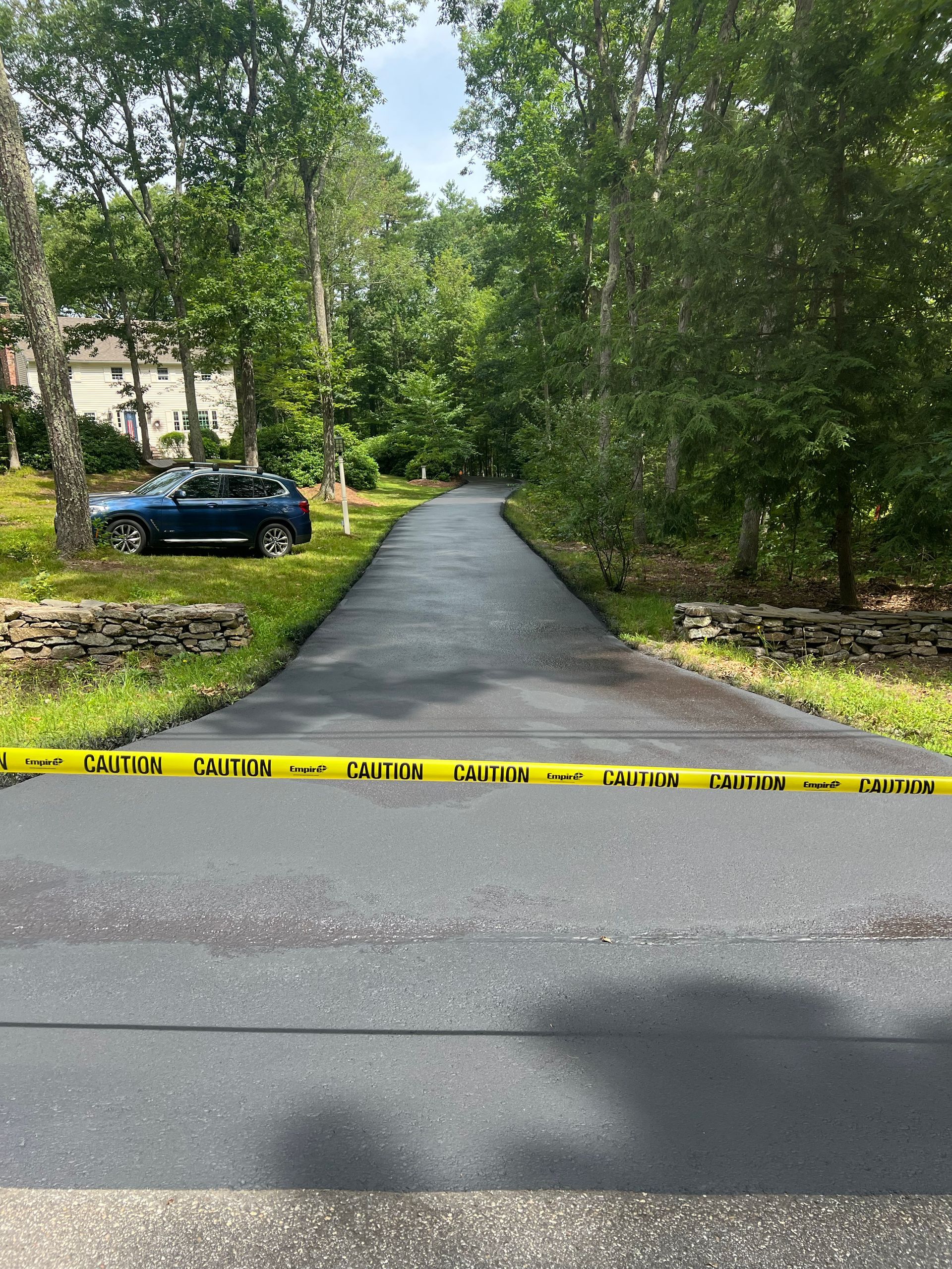 Asphalt driveway blocked by yellow caution tape; car parked on grass.