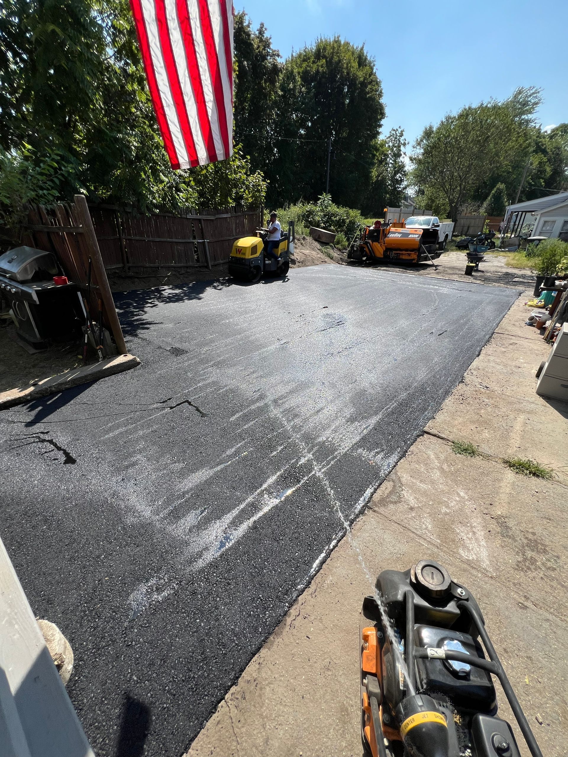 New asphalt driveway being paved, with machinery and American flag.