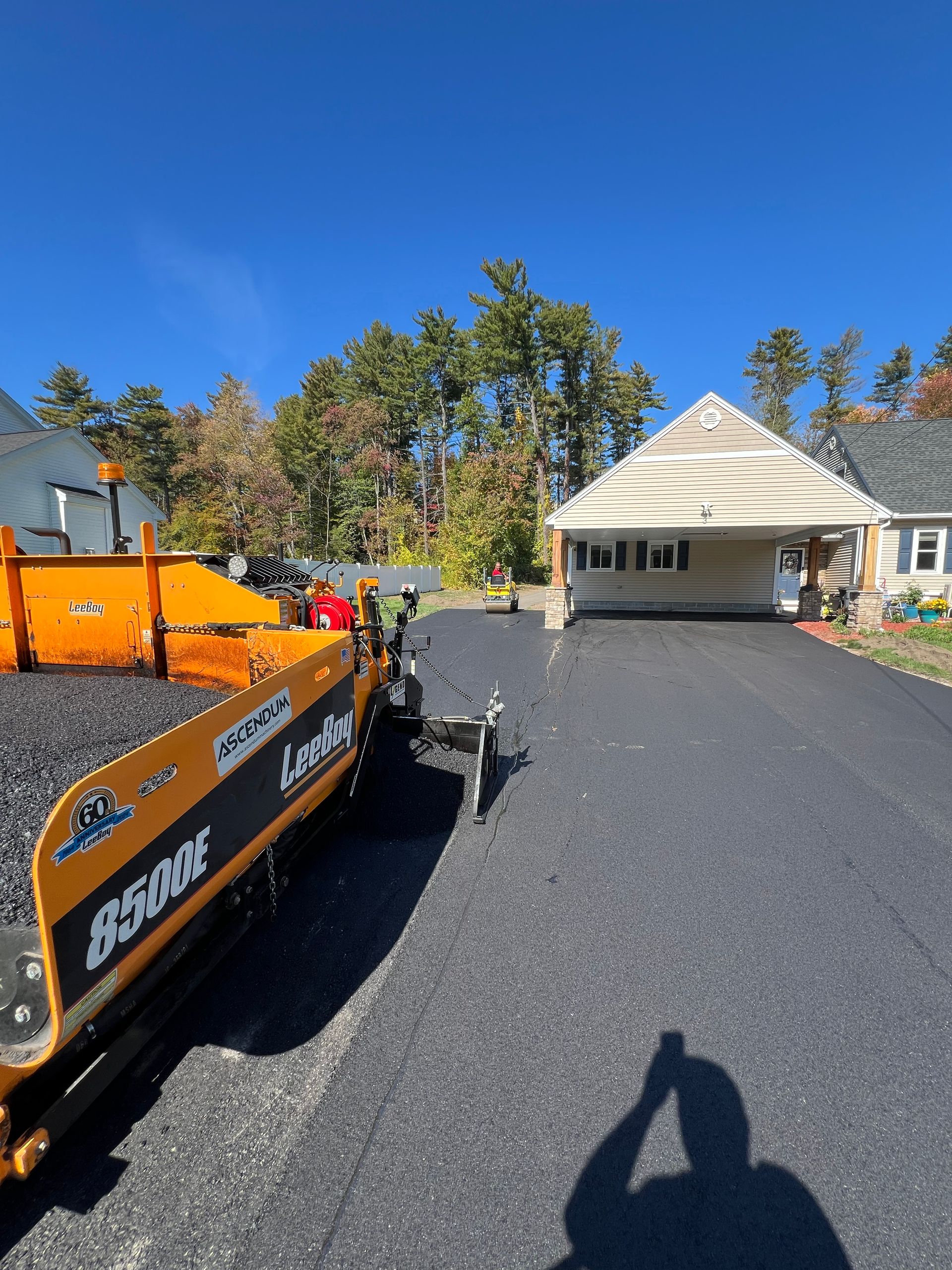 Asphalt paving machine laying black asphalt on driveway in front of a house.