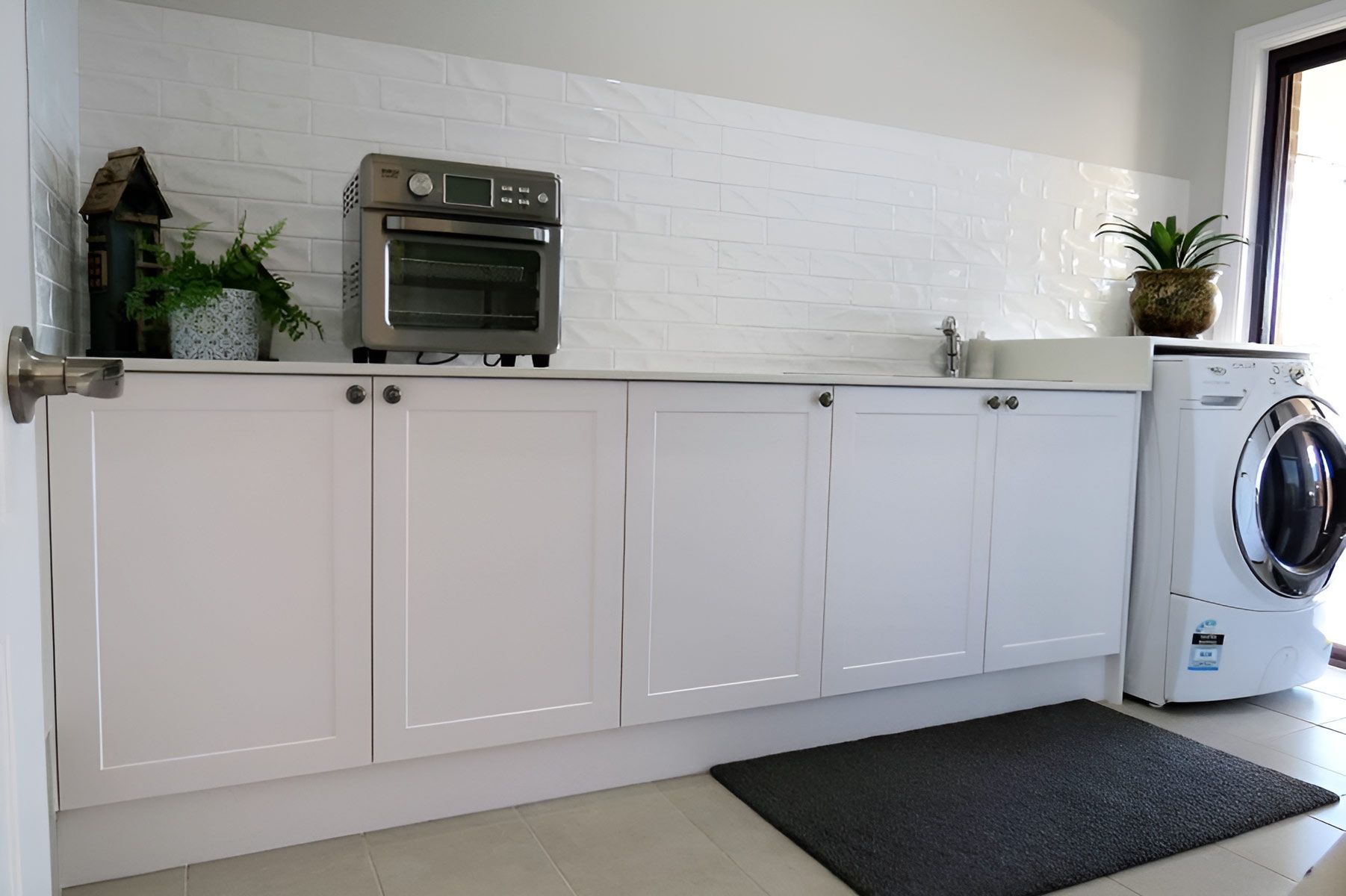 Laundry Room With White Cabinets and Plant Decor — Piscopo Kitchens Plus In Wingham, NSW