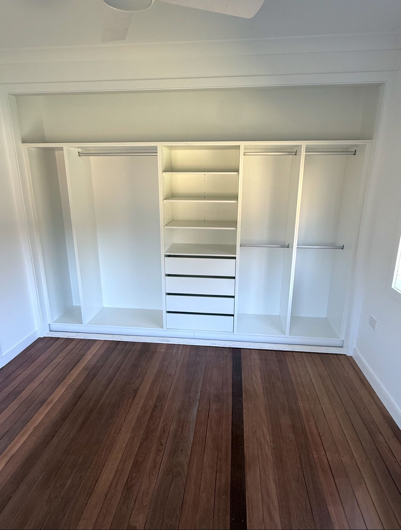 Empty Closet With Built-in White Shelving and Drawers, Wood Floor, and White Walls— Piscopo Kitchens Plus In Forster, NSW