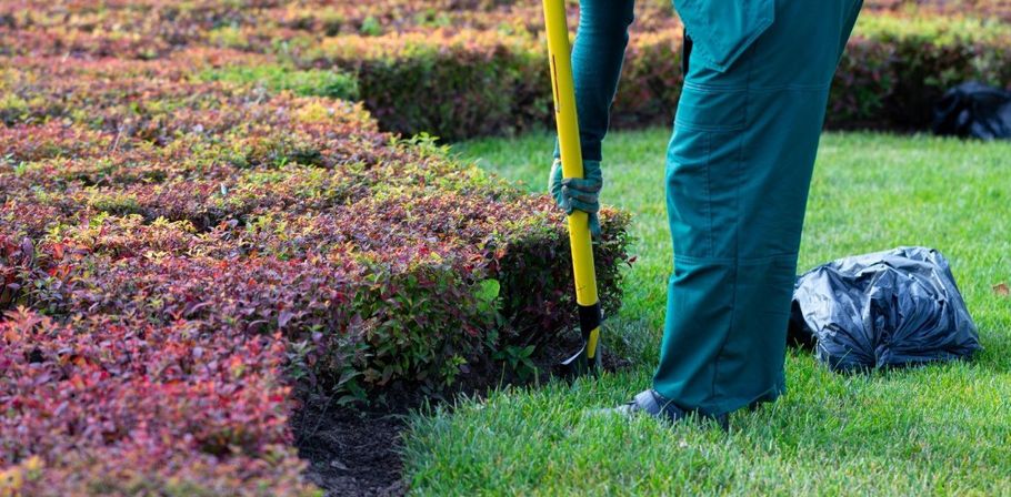 Person using a shovel to edge a colorful garden bed beside a grassy lawn