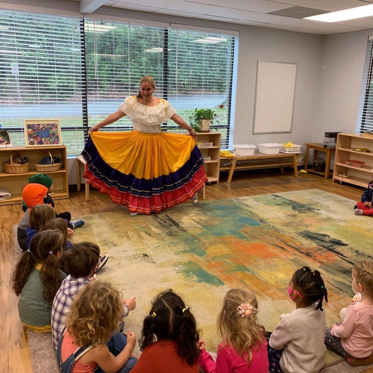 a Montessori  guide in a yellow and blue skirt is standing in front of a group of children