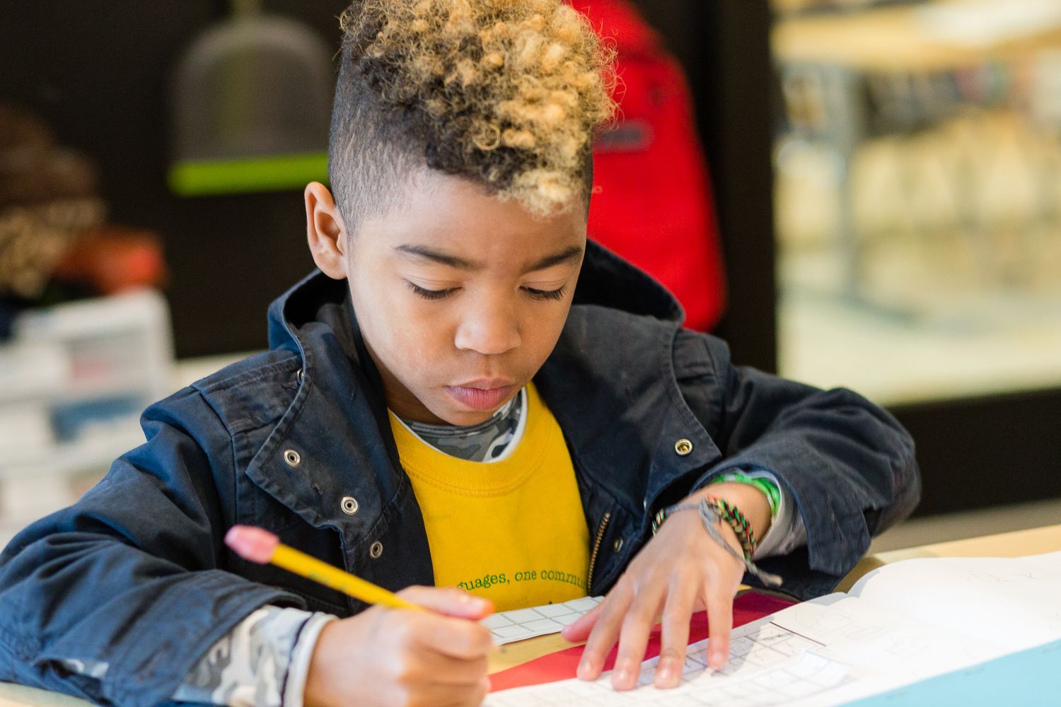 a Montessori child is sitting at a table writing on a piece of paper with a pencil