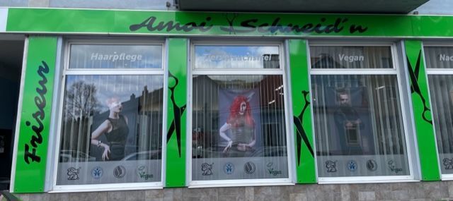 Ein grün-weißer Friseursalon mit einer Frau im Fenster.