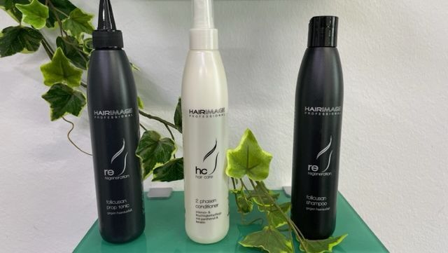 Auf einem grünen Tisch stehen drei Flaschen mit Haarpflegeprodukten.