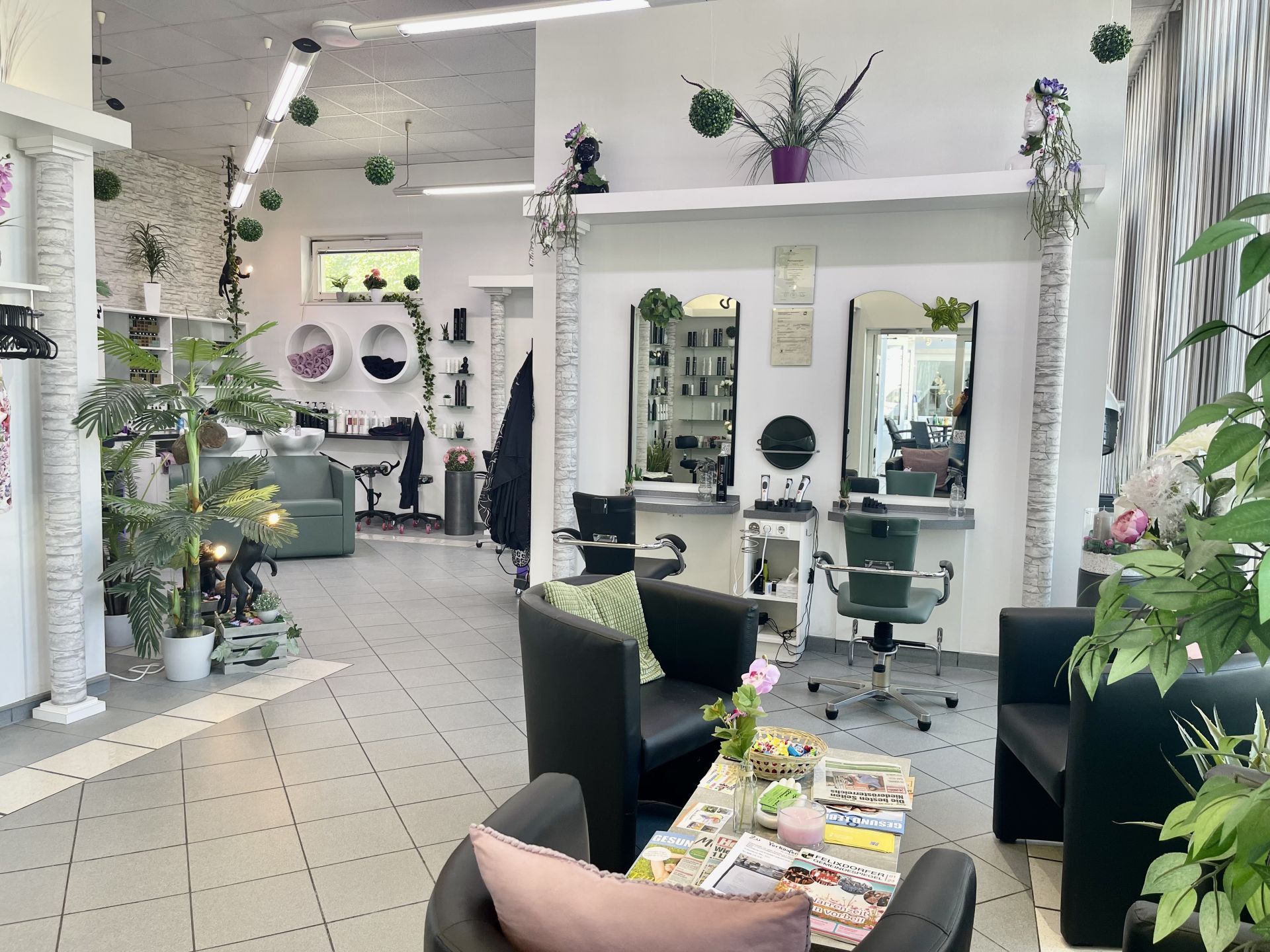 Ein Salon mit Stühlen, Tischen, Spiegeln und Pflanzen.