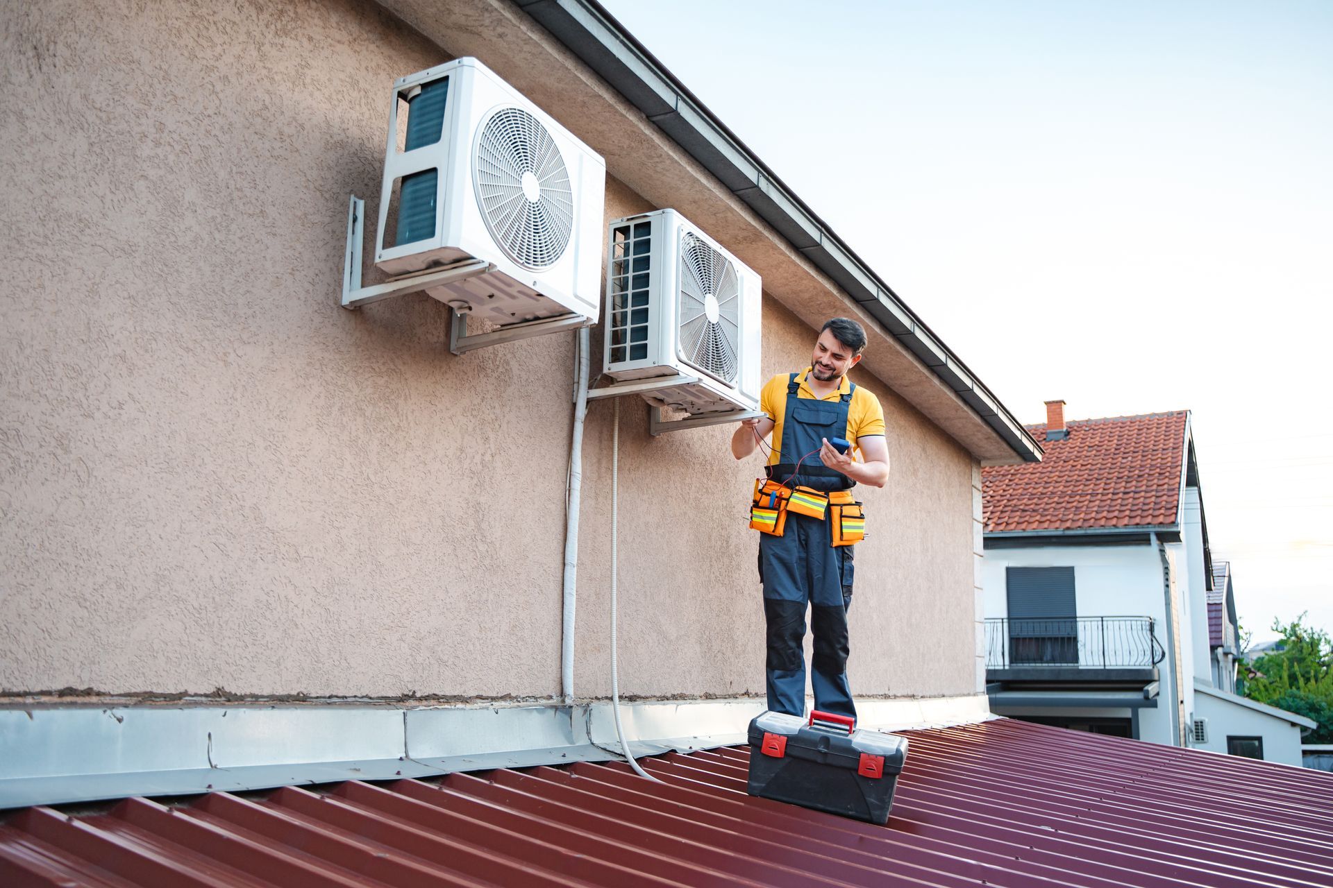 A technician using a smartphone is installing two air conditioning units on a roof. A technician using a smartphone is installing two air conditioning units on a roof.
