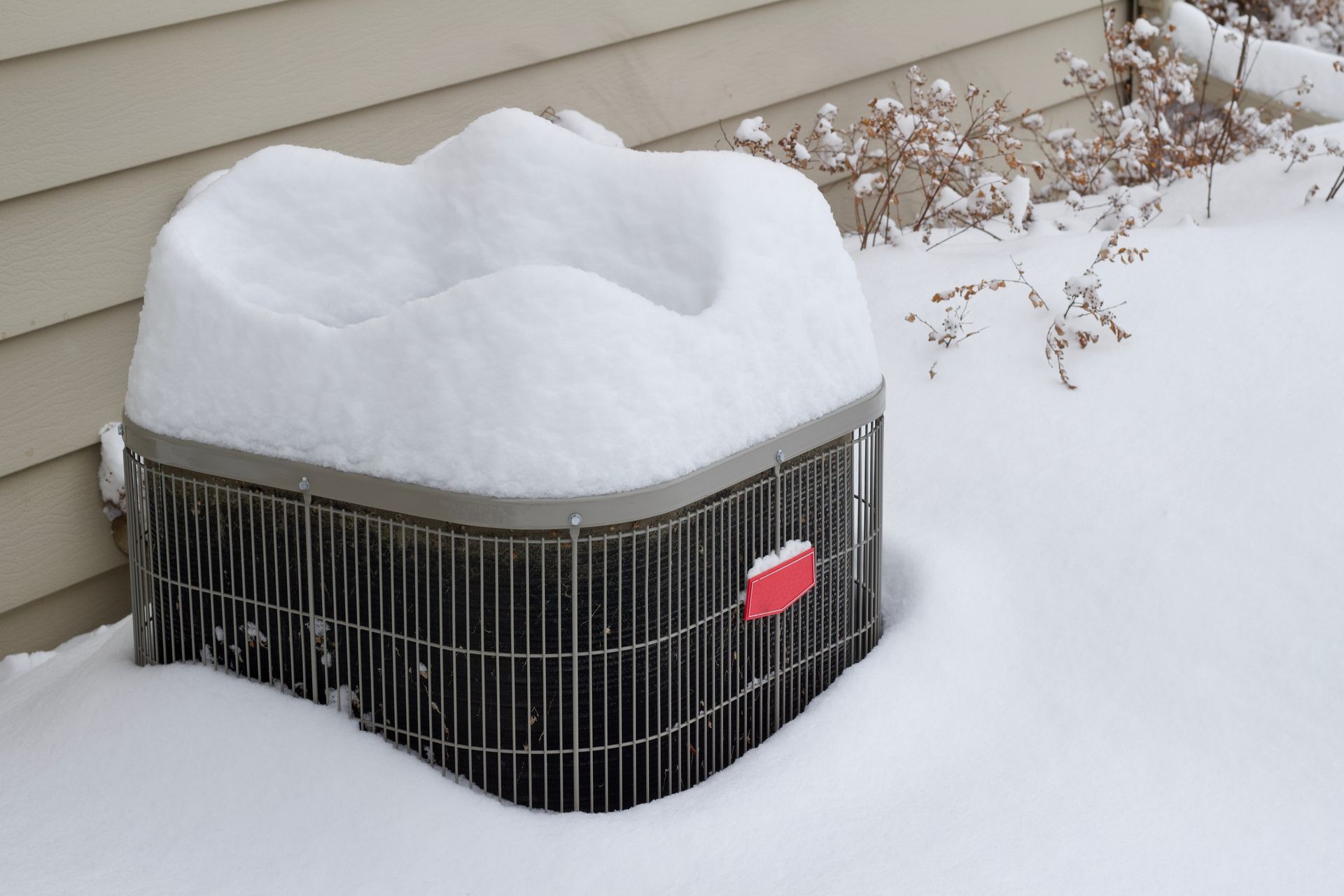 An outdoor home air conditioner unit covered with deep snow in winter.