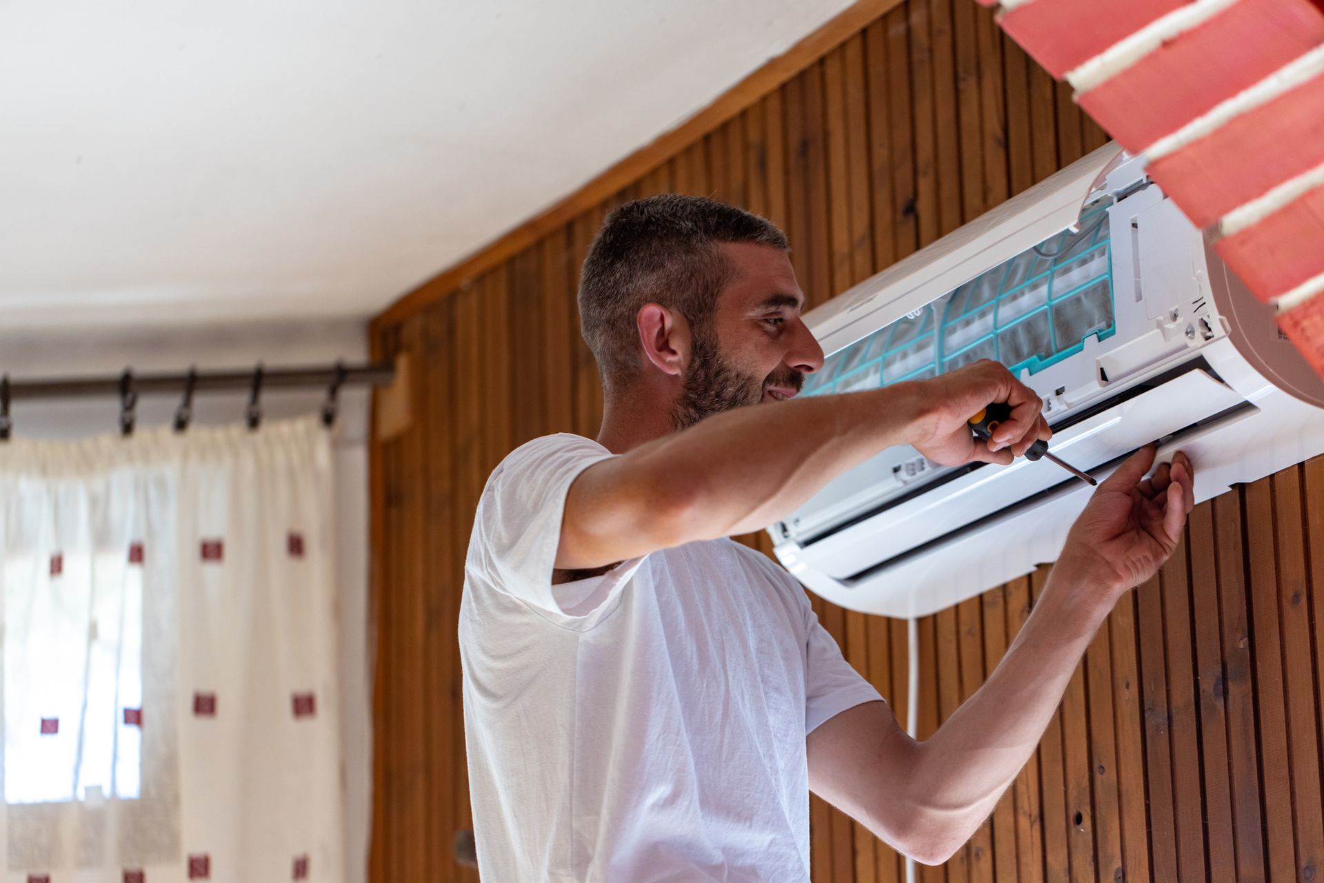 A technician using a screwdriver to tighten the screws that hold together parts of an air conditioner.