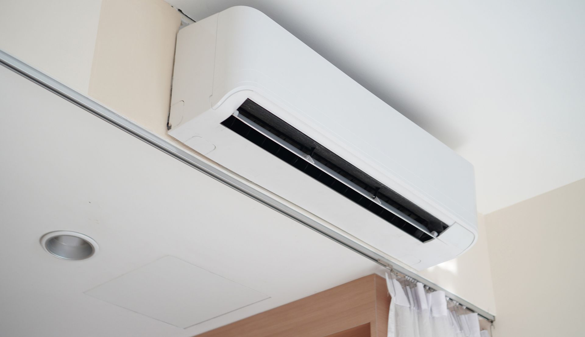 White wall-mounted air conditioner near a ceiling and curtain in a room.