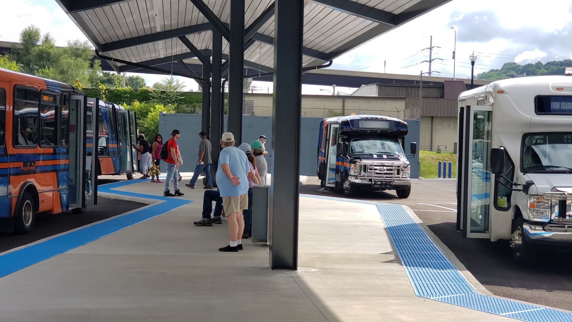 People waiting at a covered bus stop as buses arrive, with blue platform accents.