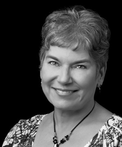 Black-and-white headshot of a smiling woman in a patterned blouse and necklace