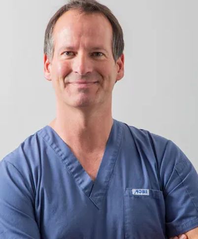 Healthcare worker in blue scrubs smiling against a light gray background
