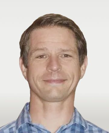 Head-and-shoulders portrait of a smiling person in a blue plaid shirt against a light background