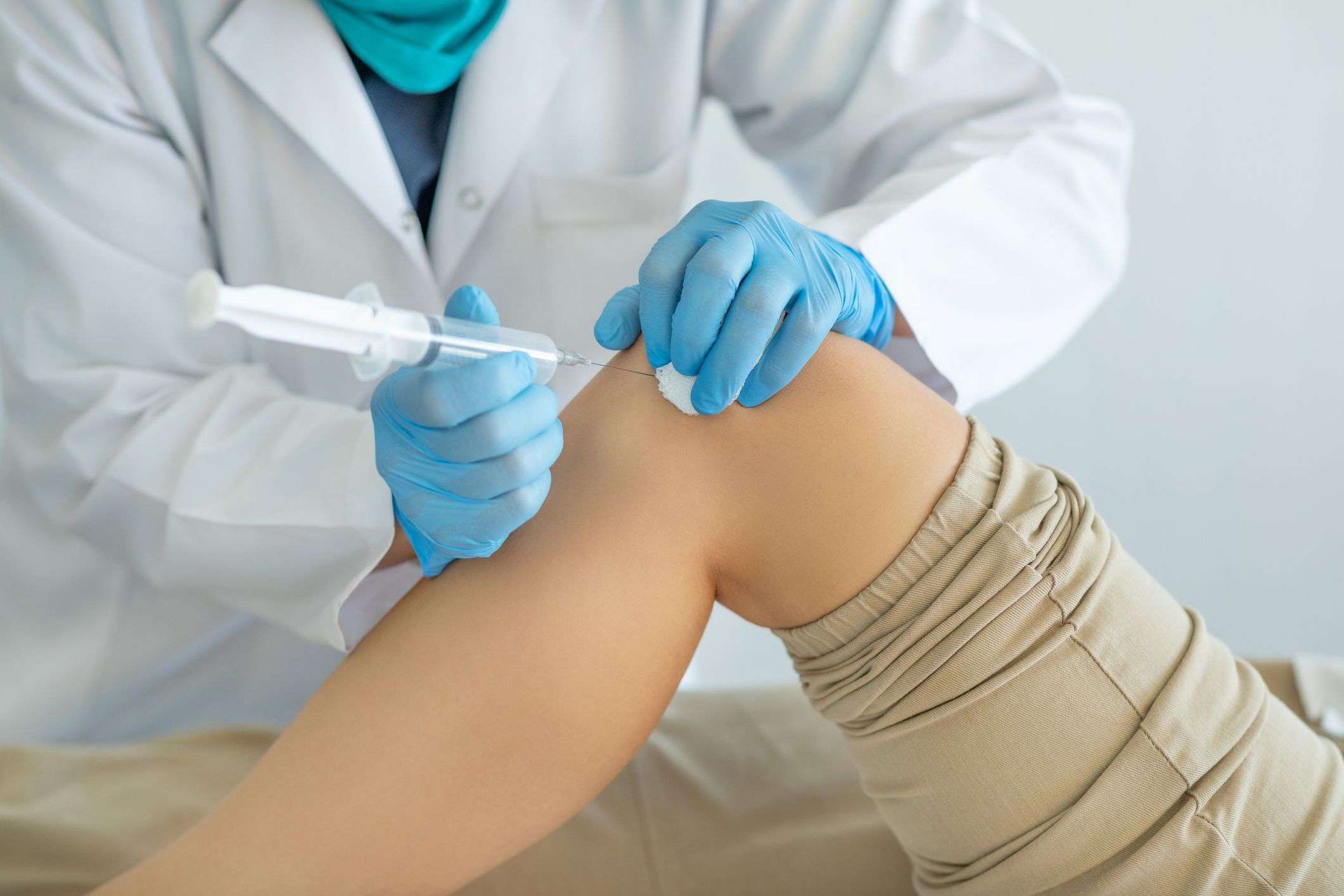 Medical professional administering an injection into a patient’s knee with gloved hands
