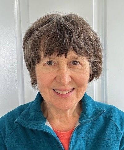 Smiling person in a teal jacket against a light background