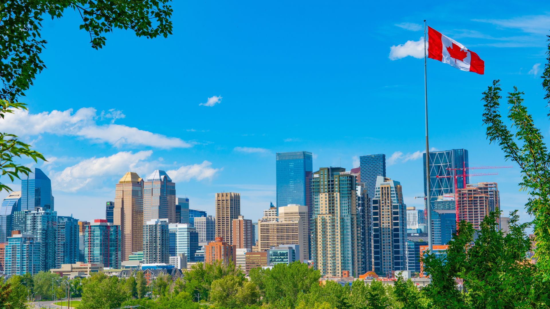 Canadian city skyline under a blue sky with a waving red-and-white flag in the foreground
