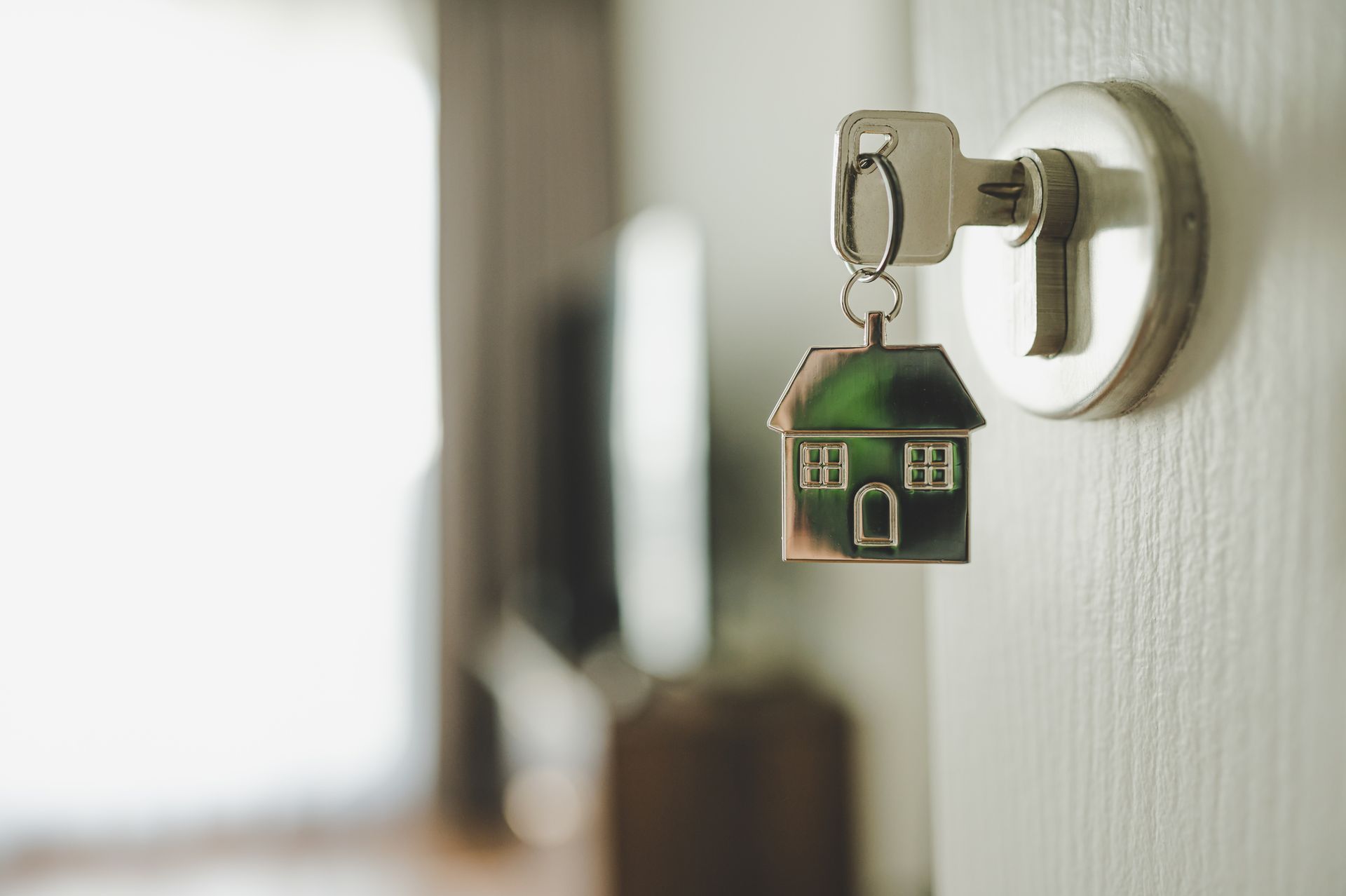 A key with a house keychain attached to it is hanging on a door. A key with a house keychain attached to it is hanging on a door.