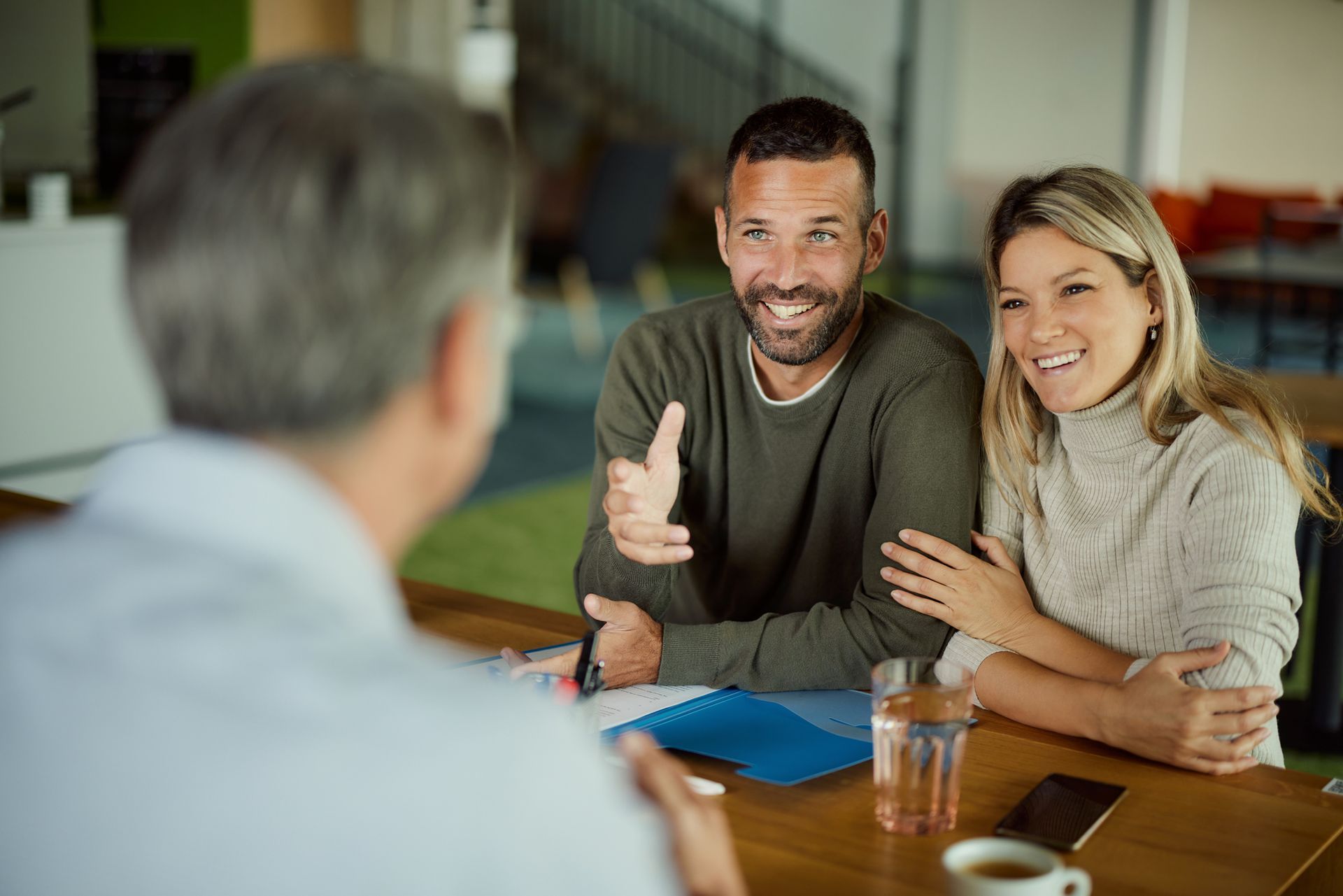 A man and a woman are sitting at a table talking to a man.