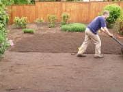 Man rolls a lawn roller over freshly turned soil in a yard.