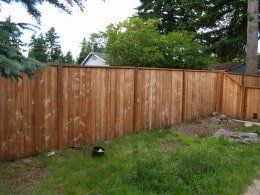 Wooden fence in front of green grass, with trees and a house in the background.