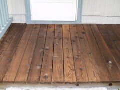Wooden deck planks in front of a window, stained brown.
