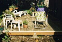 Backyard deck with lawn chairs, potted plants, and a sun lounger.