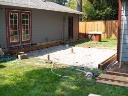 Backyard patio under construction with gravel base and house in the background.