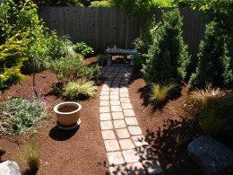 Brick pathway through a garden with a stone bench at the end.