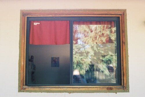 Sliding glass window with red curtain, reflecting trees.