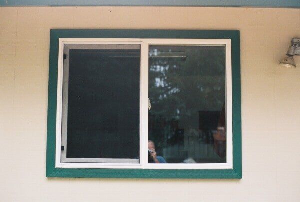 Sliding window on beige wall with green trim and white frame.