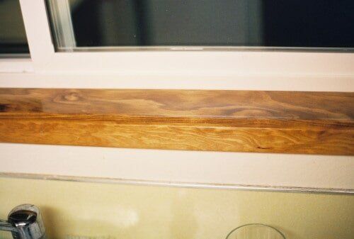 Wooden windowsill below a window, with a shiny metal faucet visible below.