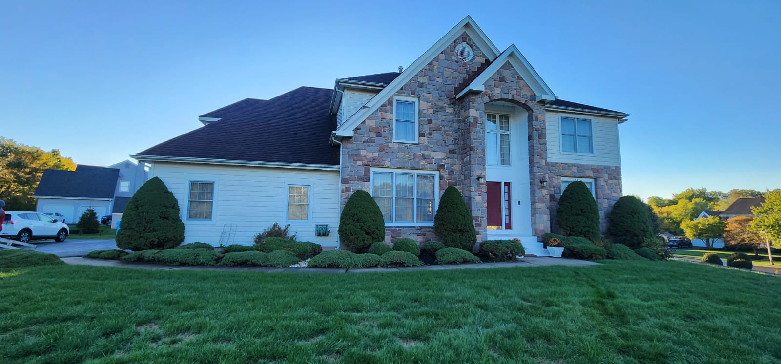 A two-story house with stone facade, red door, and manicured lawn under a blue sky.
