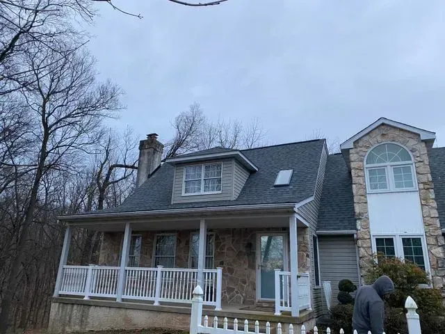 House with stone facade, covered porch, and grey roof under an overcast sky.