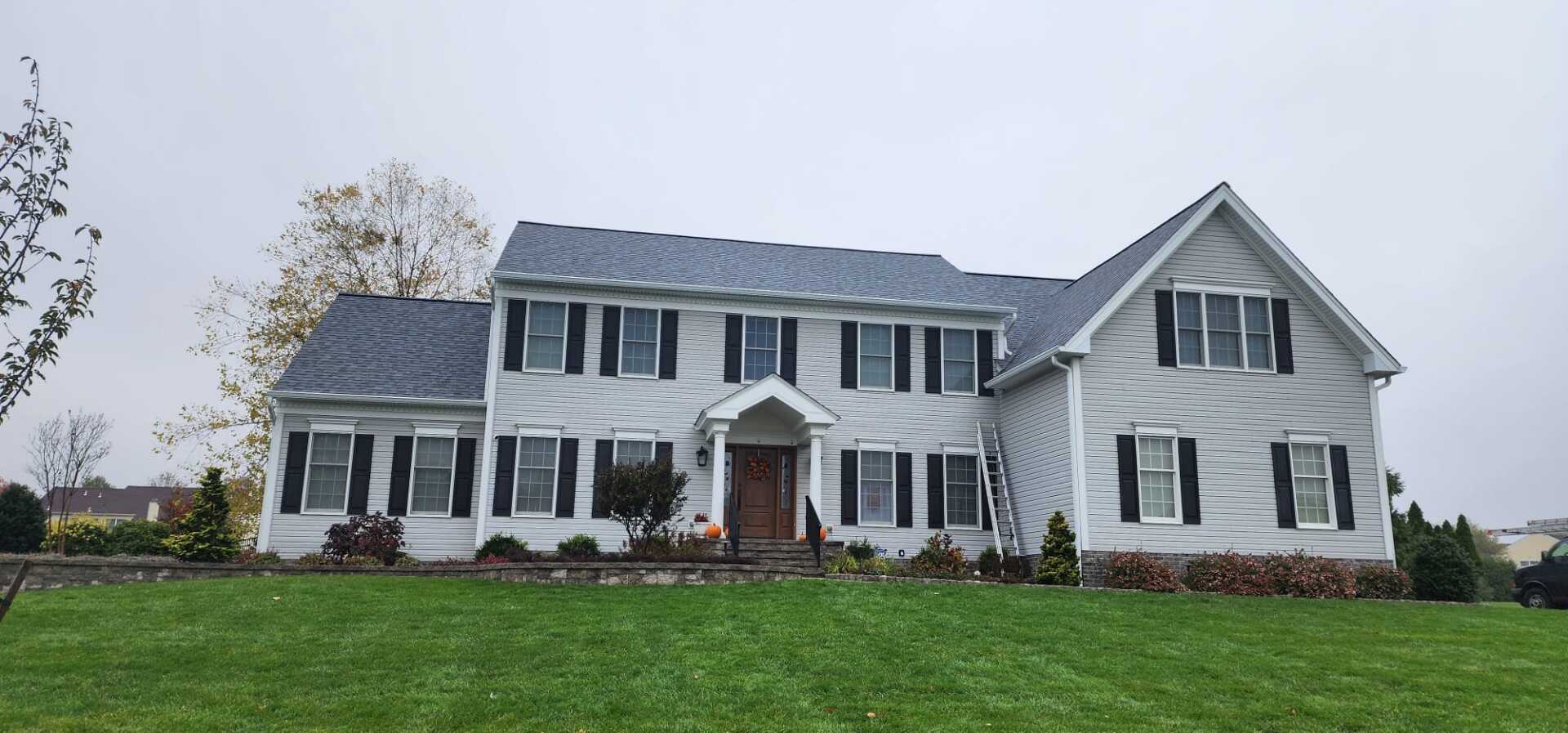 A large, two-story house with a green lawn. Gray siding, black shutters, and a gray roof. Overcast sky.