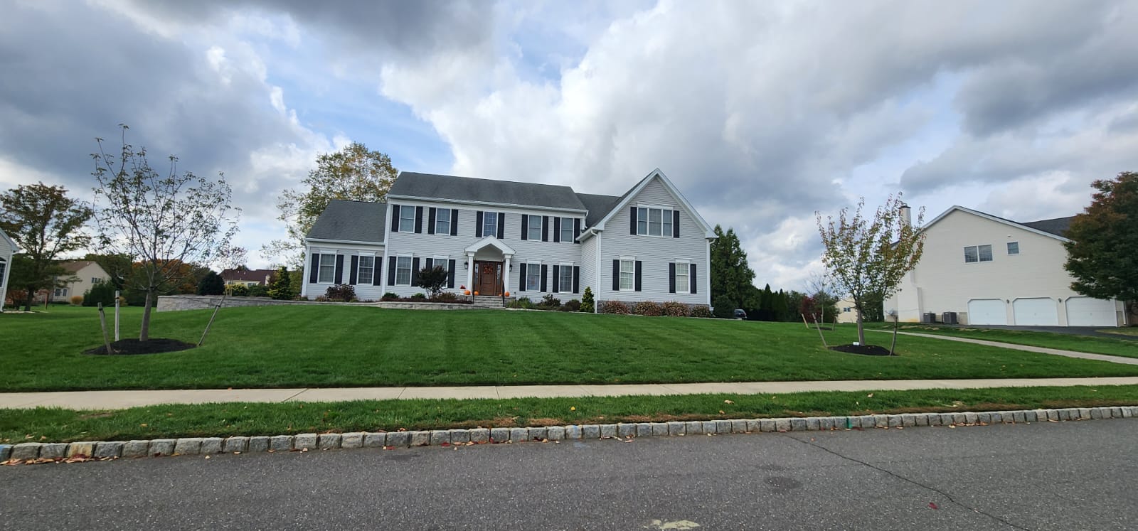 White house with black shutters, green lawn, cloudy sky.