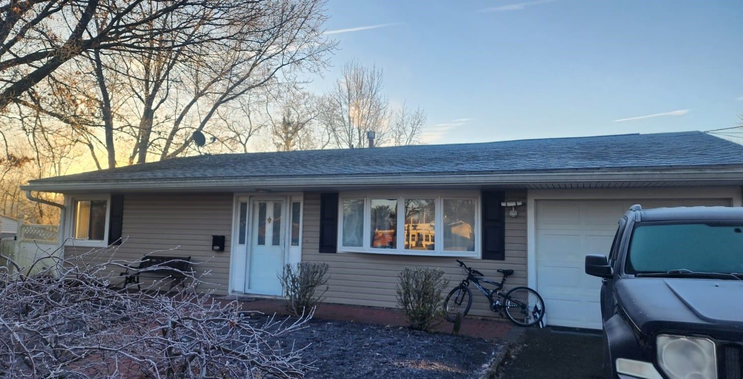 Tan ranch-style house with icy roof, black shutters, and parked bicycle. Blue car parked in front of garage.
