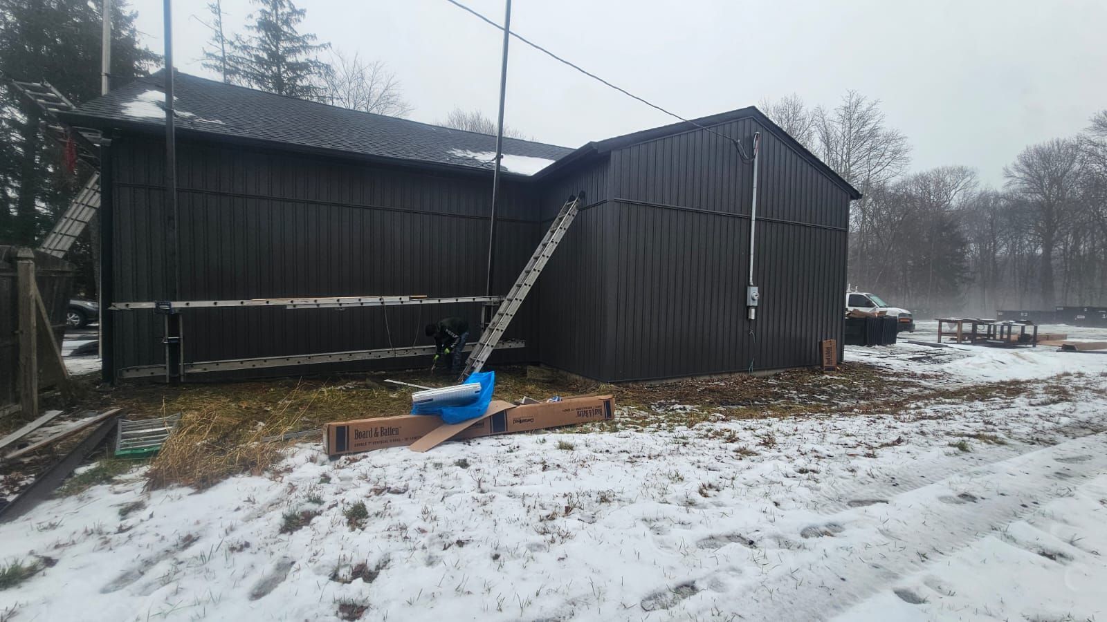 Snowy view of a dark wooden shed with a ladder leaning against the roof.