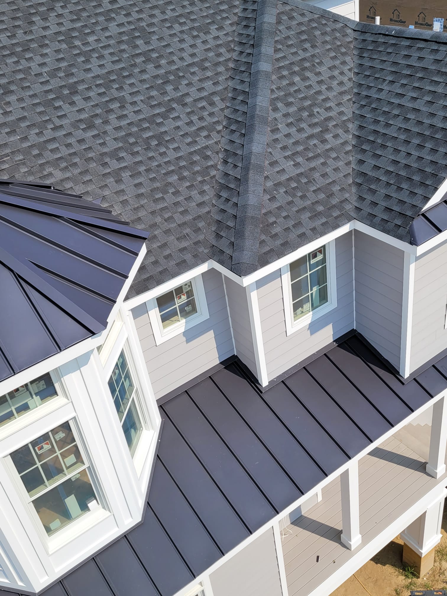 New house with a gray shingle roof and a dark metal roof section.