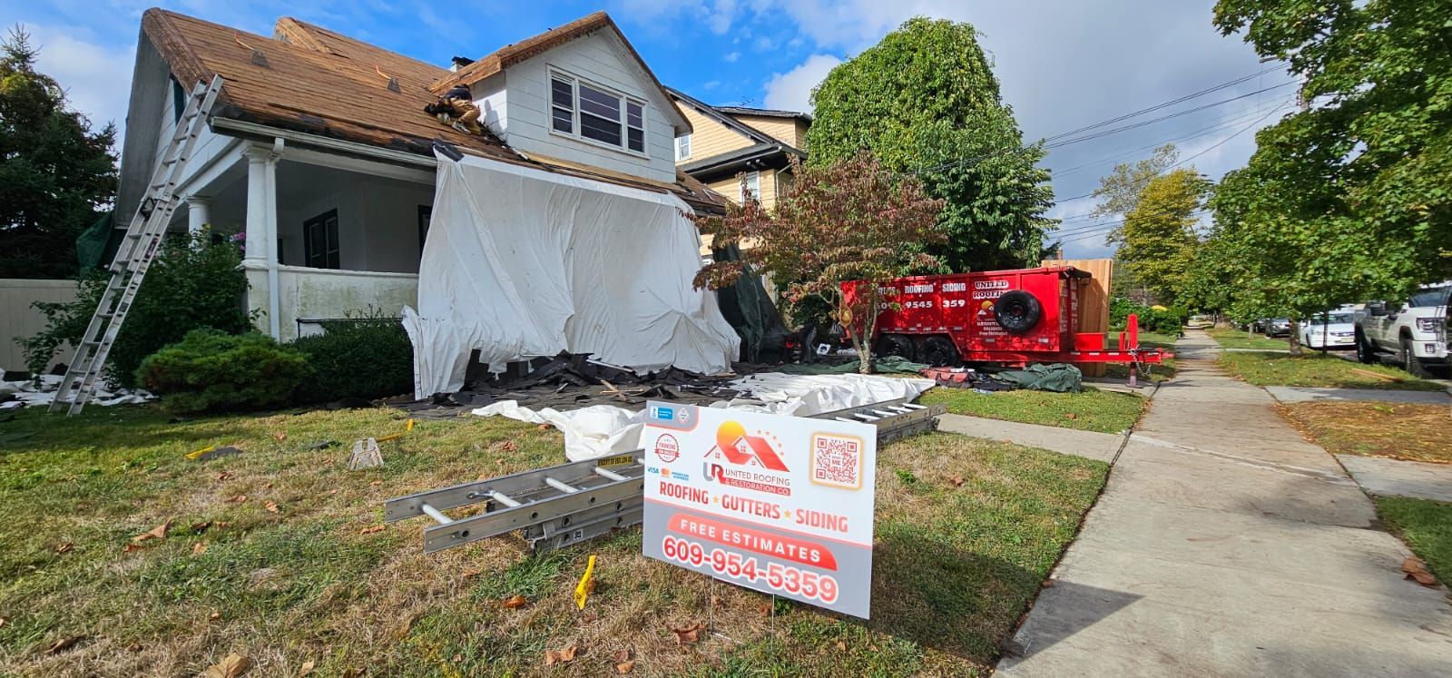 House under construction with tarp, ladder, and a repair company sign on the lawn.