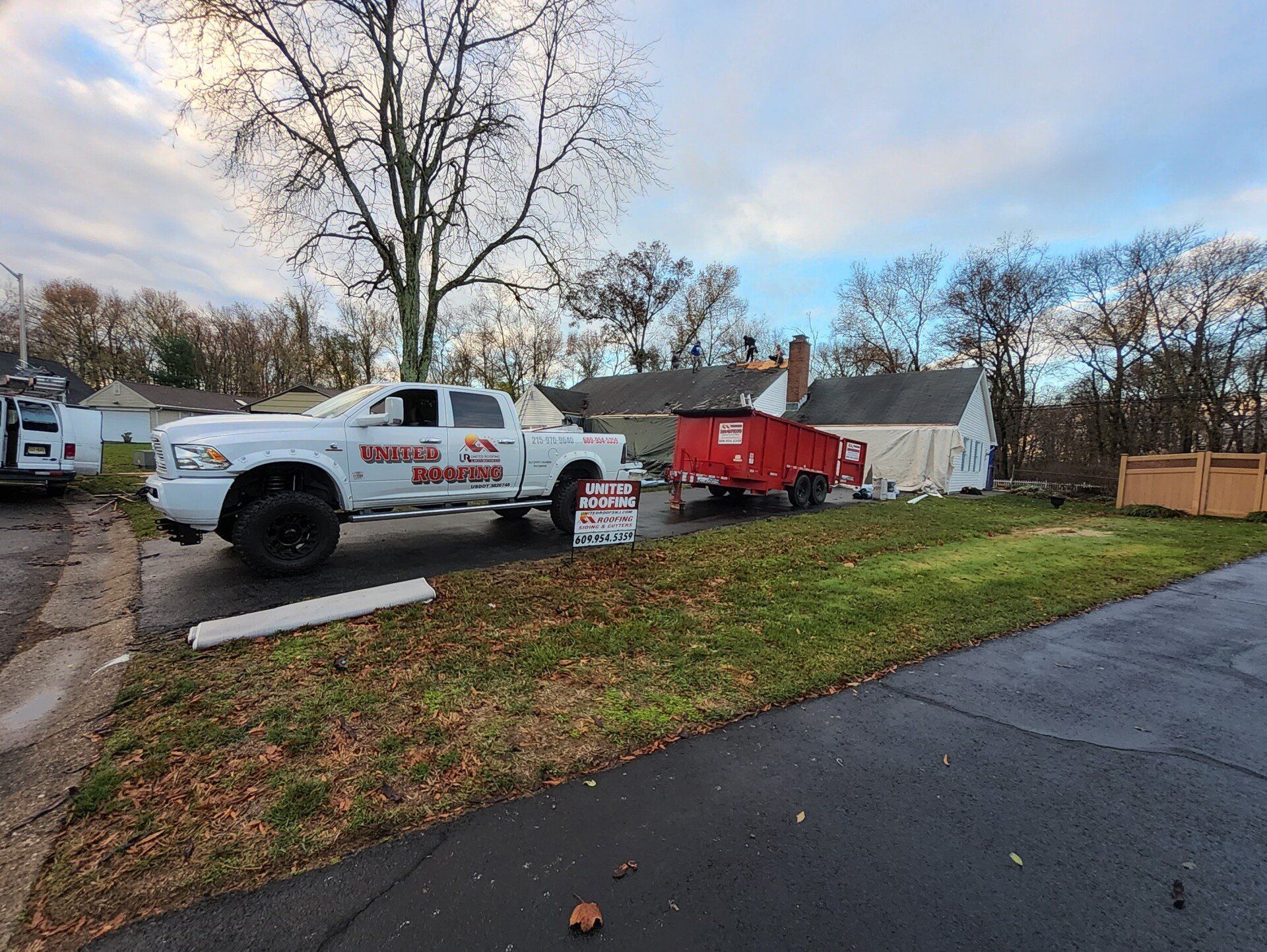 White truck and red trailer parked in front of a house, sign in the yard. Overcast sky.