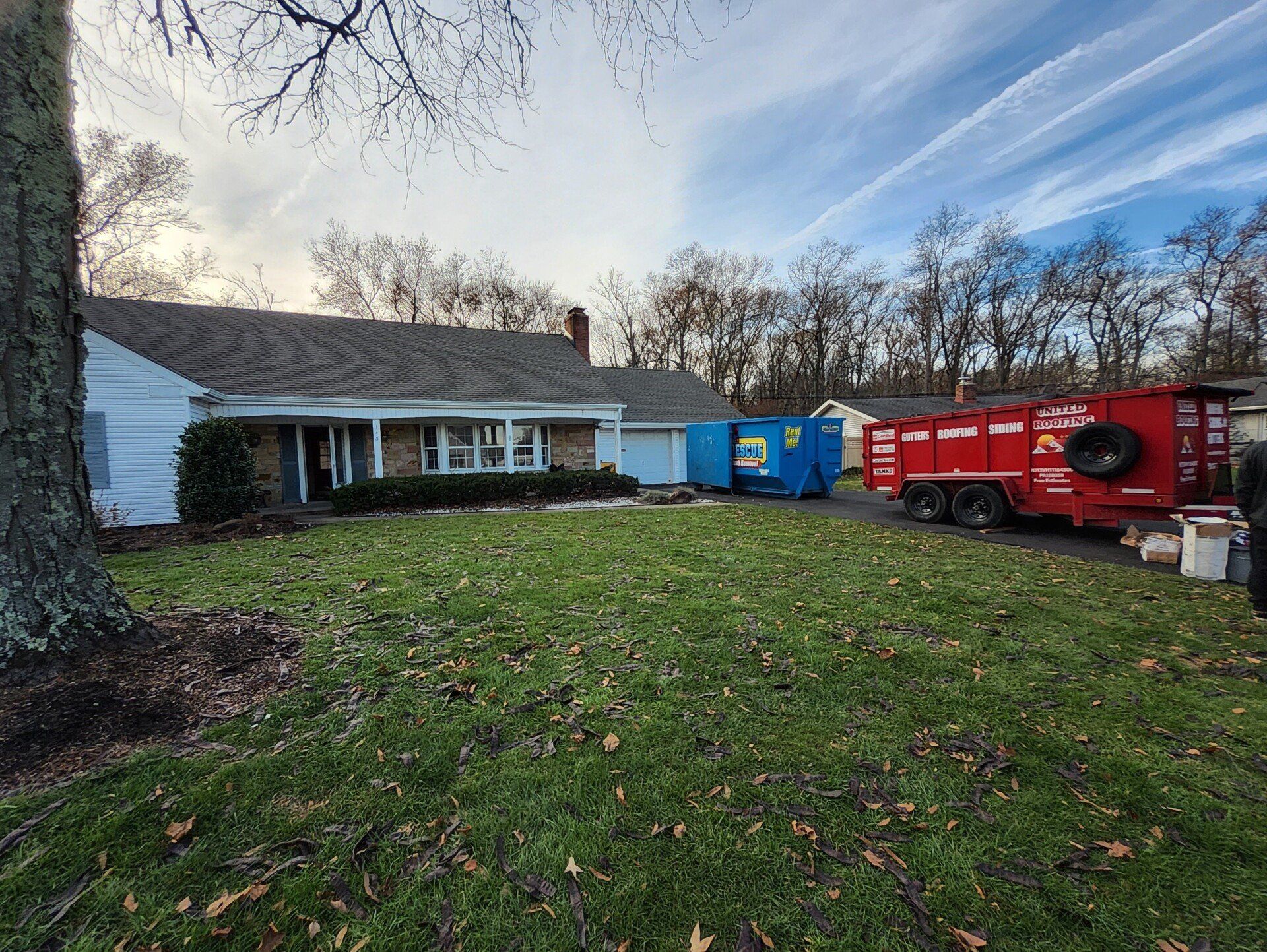 House with roof work underway; blue and red dumpsters on the lawn.