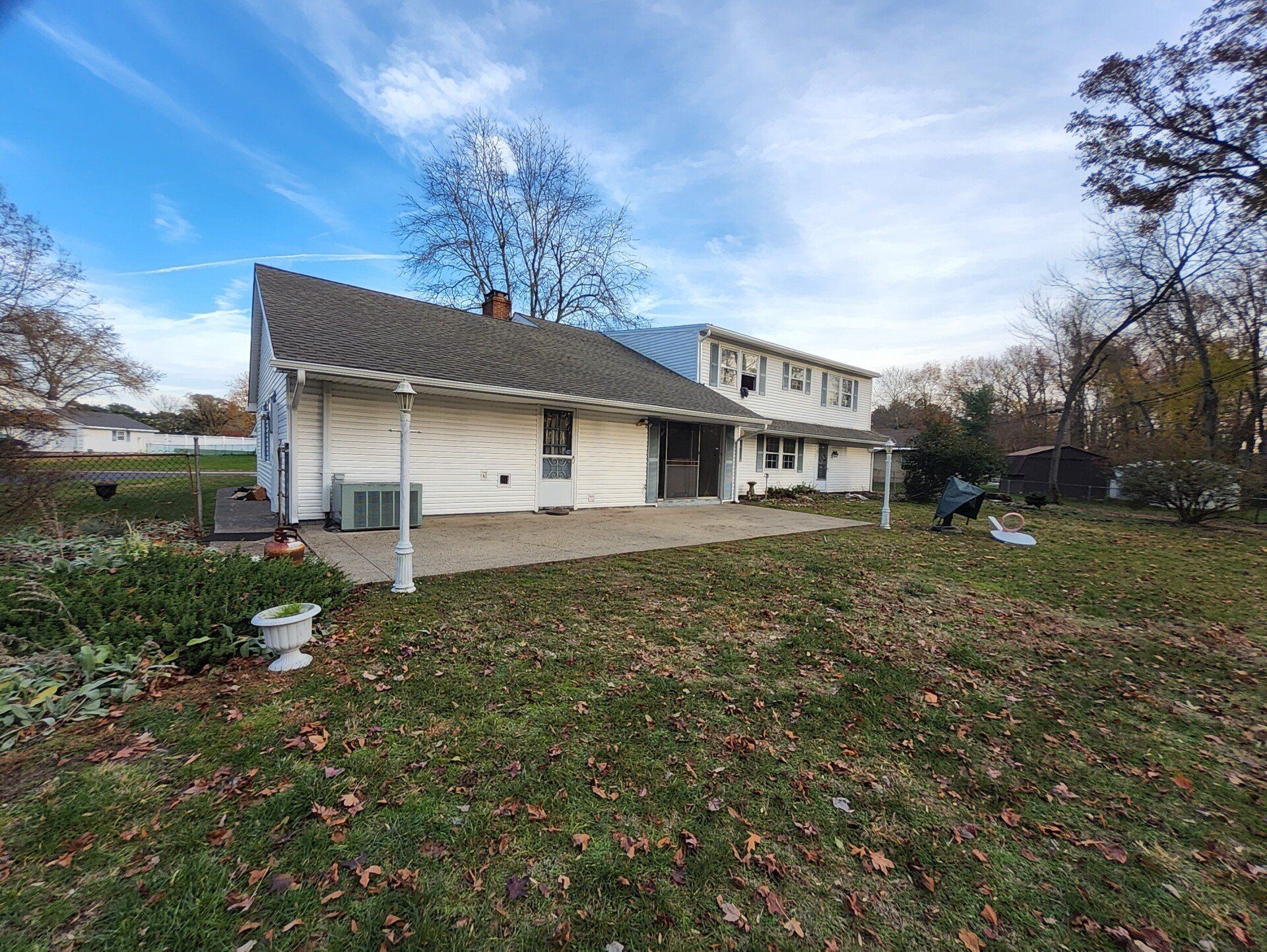 House with white siding and a partially constructed roof under a blue sky. Yard with autumn leaves.