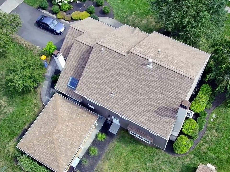 Aerial view of a brown-roofed house with a car parked in the driveway and green landscaping.