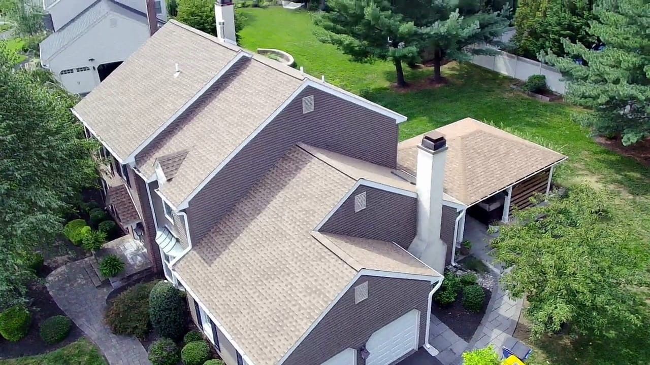 Aerial view of a brown-roofed house with white trim, a driveway, and surrounding green lawn.