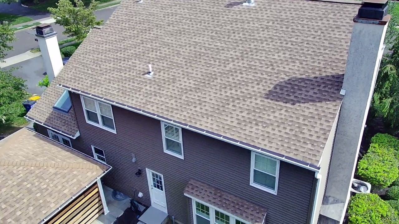 Brown roof of a two-story house with brown siding and white-framed windows, viewed from above.